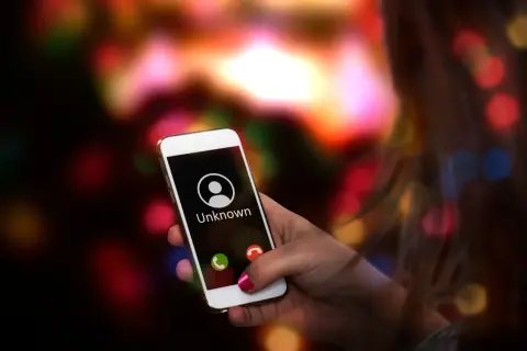 Dłoń trzyma smartfon Samsung z ekranem pokazującym przychodzące połączenie od nieznanego numeru. Chcesz wiedzieć, jak wyłączyć numer prywatny Samsung?