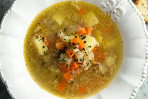 Zupa warzywna w białej misce z ziemniakami, marchewką i szczypiorkiem.