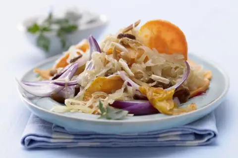 Ein Teller mit gebratenem Sauerkraut, garniert mit roten Zwiebeln, Rosinen und Mandelsplittern.