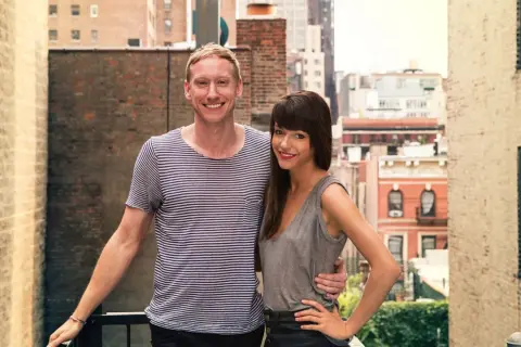 Jessica Walsh and her partner, perhaps celebrating a milestone in her most famous work, stand on a rooftop with a city skyline behind them.