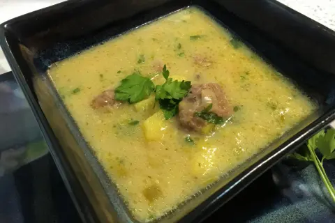 Aksamitna zupa porowo serowa z pulpecikami, ozdobiona natką pietruszki, w kwadratowej misce.