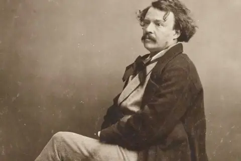 Portrait photographique 19ème siècle d'un homme à la moustache et aux cheveux bouclés, vêtu d'un manteau sombre et d'une chemise à nœud.