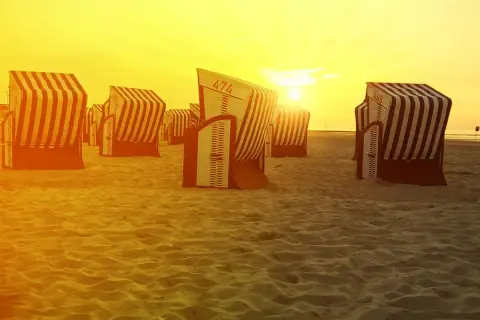 Zachód słońca nad plażą na Morzu Północnym w Niemczech. Puste kosze plażowe czekają na gości.