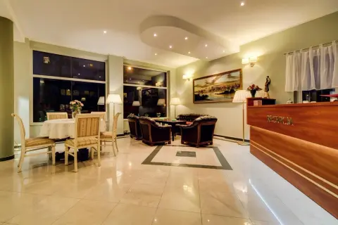 Eleganckie wnętrze recepcji Villa Plaza Warszawa. Wygodne fotele, stolik z kwiatami i luksusowy lada.