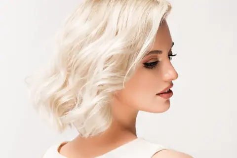 Kobieta z krótkimi, blond falowanymi włosami i makijażem.