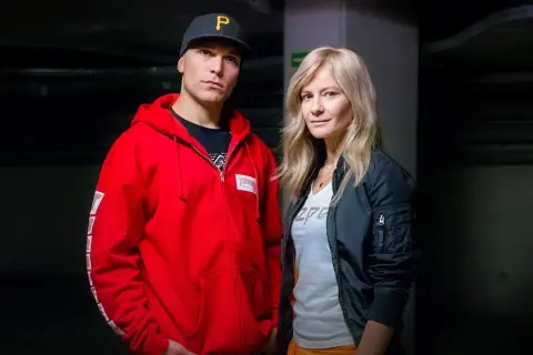 Tomasz Chada z żoną, w ciemnym korytarzu. On w czerwonej bluzie i czapce, ona w czarnej kurtce.