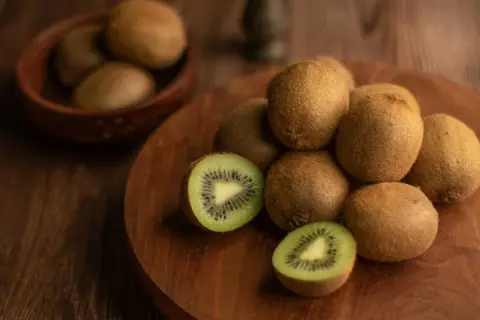 Kiwi, noti per essere tra i cibi che fanno andare in bagno, sono disposti su un tagliere di legno. Uno è tagliato a metà, mostrando la polpa verde e i semi neri.