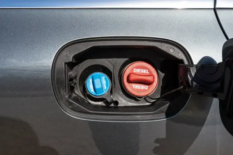 Dwa korki wlewu paliwa samochodu: niebieski z napisem AdBlue i czerwony z napisem Diesel.