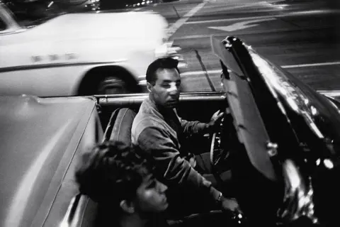 Garry Winogrand uchwycił nocną jazdę kabrioletem. Mężczyzna za kierownicą, kobieta obok. Rozmyte światła miasta.