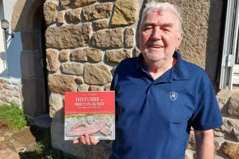 Un homme souriant tient un livre sur l'histoire du breton écrit. Son nom de famille breton est Favreau.