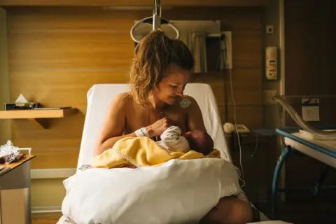 Nybliven mamma ammar sitt barn på en sjukhussäng. En lugn stund efter förlossningen, kanske inför en efterkontroll på MVC.
