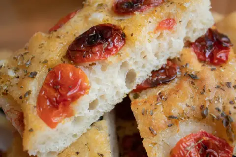 Nahaufnahme von Focaccia, einem der beliebtesten italienischen Brotsorten, mit getrockneten Tomaten und Kräutern bestreut.