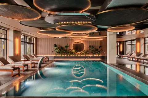 Luksusowy basen w karpacz hotel spa. Woda lśni, otoczona leżakami i zielenią. Nowoczesny design sufitu z podświetleniem.