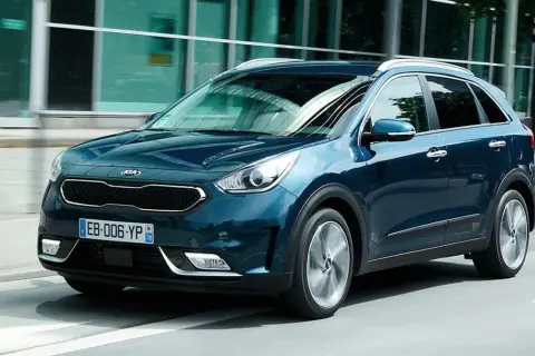 Ciemnoniebieski Kia Niro jedzie ulicą obok nowoczesnego budynku.