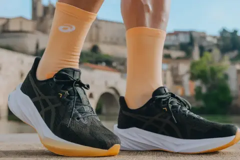 Biegacz w pomarańczowych skarpetkach z logo Asics i ciemnych butach tej firmy, gotowy do podboju świata. Asics co to za firma? To synonim jakości w sporcie.