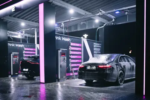 Nowoczesna bezdotykowa myjnia samochodowa Pink Wash nocą. Czarne samochody pokryte pianą, lśniące od wody podłogi i neonowe światła tworzą futurystyczny klimat.