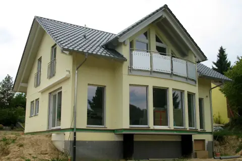 Nowoczesne projekty domów z poddaszem, żółty dom z dużymi oknami i balkonem, w trakcie budowy.