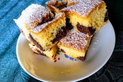 Ein saftiger versunkener Streuselkuchen mit Marmormuster, bestäubt mit Puderzucker, liegt auf einem Teller.