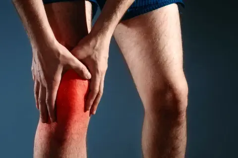 Mężczyzna trzyma się za zaczerwienione kolano, odczuwając nieprzyjemne szczypanie w kolanie.