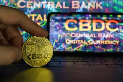 Złota moneta z napisem CBDC w dłoni na tle ekranu z wykresem i napisem "Central Bank Digital Currency". To przyszłość finansów, ale cbdc co to?