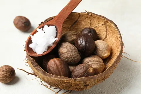 Noci di karité in una ciotola di cocco, con un cucchiaio di burro bianco. Il burro di karité serve per nutrire e idratare la pelle.