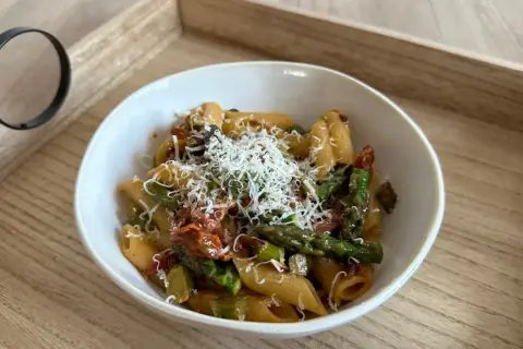 Makaron penne z zielonymi szparagami i suszonymi pomidorami, posypany parmezanem.
