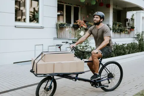 Mann liefert Pakete mit einem Lastenrad. Eine gute Lastenrad Versicherung schützt vor unerwarteten Schäden.