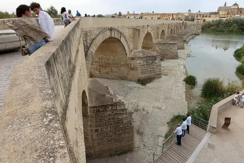 Gente admira el puente romano de Córdoba. Para llegar, sigue el río Guadalquivir.