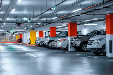 Jasne, oto opis alternatywny:

Rząd samochodów zaparkowanych pod jasnym oświetleniem parkingu. Kolorowe słupy i strzałki kierunkowe wskazują drogę.