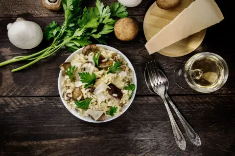 Risotto ai funghi cremoso, guarnito con prezzemolo fresco e scaglie di parmigiano. Un bicchiere di vino bianco completa questo perfetto abbinamento vino funghi.