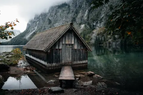 Alte Holzhütte am Ufer des Obersee-Sees, umgeben von steilen Felswänden und nebliger Atmosphäre.
