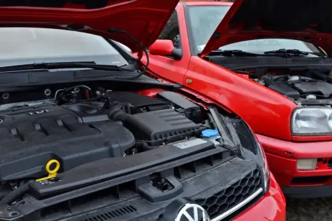 Dwa czerwone Volkswageny z otwartymi maskami. Widać silnik TDI, czyli silnik diesla, w nowszym modelu i starszy silnik w Golfie III.