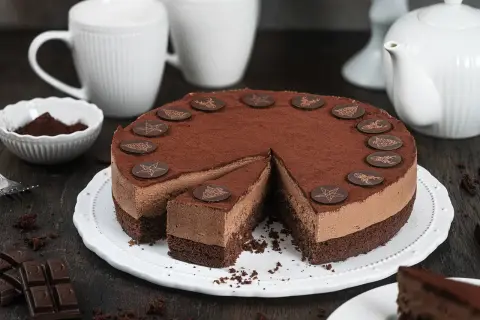 Schokocreme Torte mit Mascarpone, dekoriert mit Schokoladen-Emblemen. Ein Stück ist bereits angeschnitten.