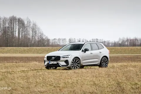 Srebrne Volvo XC60 Polestar na tle suchej trawy i drzew.