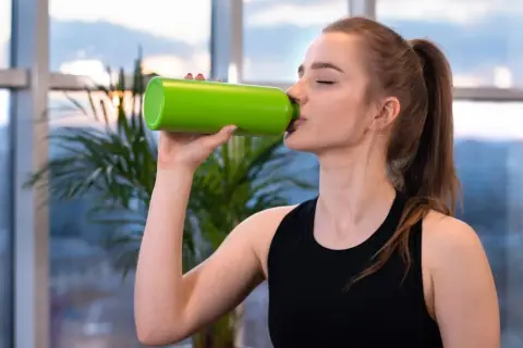 Junge Frau trinkt aus grüner Flasche. Sie fragt sich, wie viel Elektrolyte am Tag sie braucht, um fit zu bleiben.