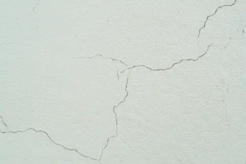 Detalle de grietas finas en una fachada de color crema, mostrando el paso del tiempo y la textura del material.