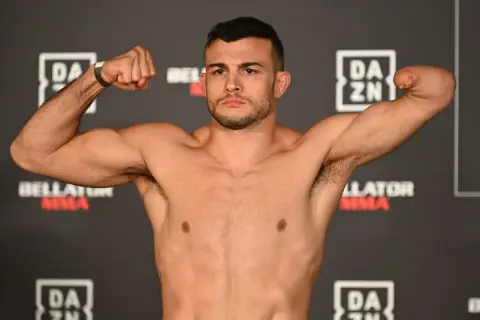 Fighter with one arm boxing, flexing his bicep. He stands against a backdrop of DAZN and Bellator MMA logos.