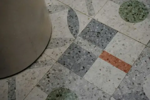 Detalle de un suelo terrazo con diseño geométrico y un pilar. El pulido del suelo terrazo resalta sus motas de colores.