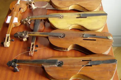 Kilka drewnianych instrumentów smyczkowych, w tym skrzypce, leżących na drewnianym stole.