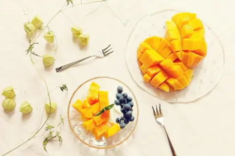 Słodkie mango pokrojone w kostkę, idealne do jedzenia z jagodami i jogurtem. Obok gałązka z zielonymi pąkami.