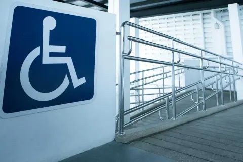 Segnale di accessibilità per disabili accanto a una rampa con corrimano, a norma con la legge 104 per l'abbattimento barriere architettoniche.