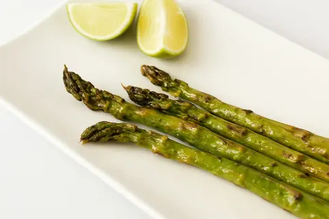 Asperges rôties sur une assiette blanche avec des quartiers de citron vert. Une idée simple pour une recette d'asperges savoureuse.
