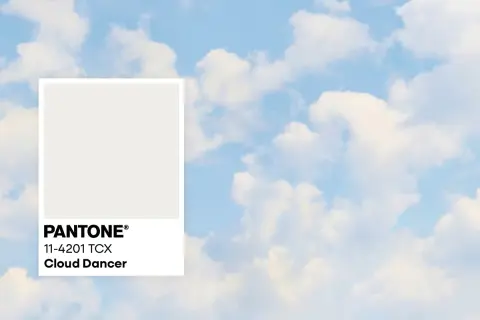 Pantone-Farbkarte "Cloud Dancer" vor einem Himmel mit Wolken. Diese zarte Farbe könnte die Farbe des Jahres 2026 sein.