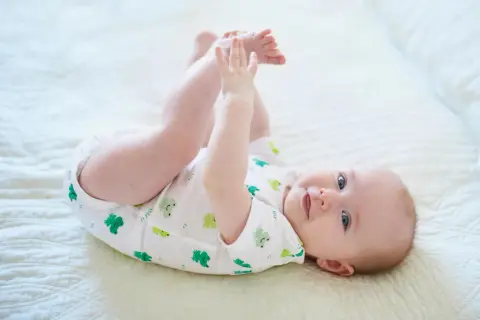 Ein Baby mit 6 Monaten kann schon viel! Dieses Baby liegt auf dem Rücken, hebt seine Beine und spielt mit seinen Füßen.