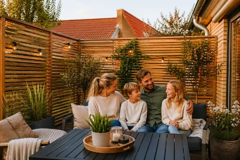 Familj njuter av kvällen på altanen, omgiven av ett vackert insynsskydd i trä.