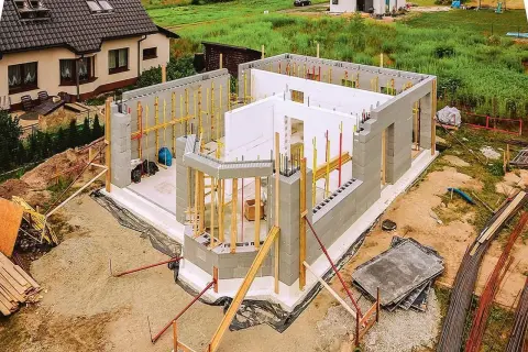 Budowa domu ze styropianu w toku. Ściany z bloczków betonowych i białego styropianu, zbrojenia i drewniane podpory.