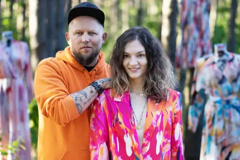 Para pozuje wśród kolorowych sukienek. Mężczyzna w pomarańczowej bluzie, kobieta w marynarce. Naoko - co to za firma?
