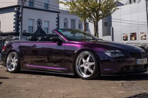 Fioletowe BMW E64 kabriolet z chromowanymi felgami stoi na ulicy.