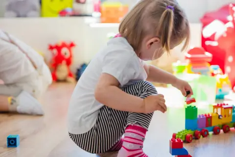 Niña de 0-3 años jugando con bloques de construcción. Crea un tren de juguete y una figura humana.