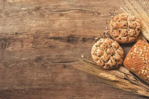 Chleb pełnoziarnisty z ziarnami i kłosy zbóż na drewnianym tle. Jaki chleb przy hashimoto? Wybieraj ten z dobrych składników.